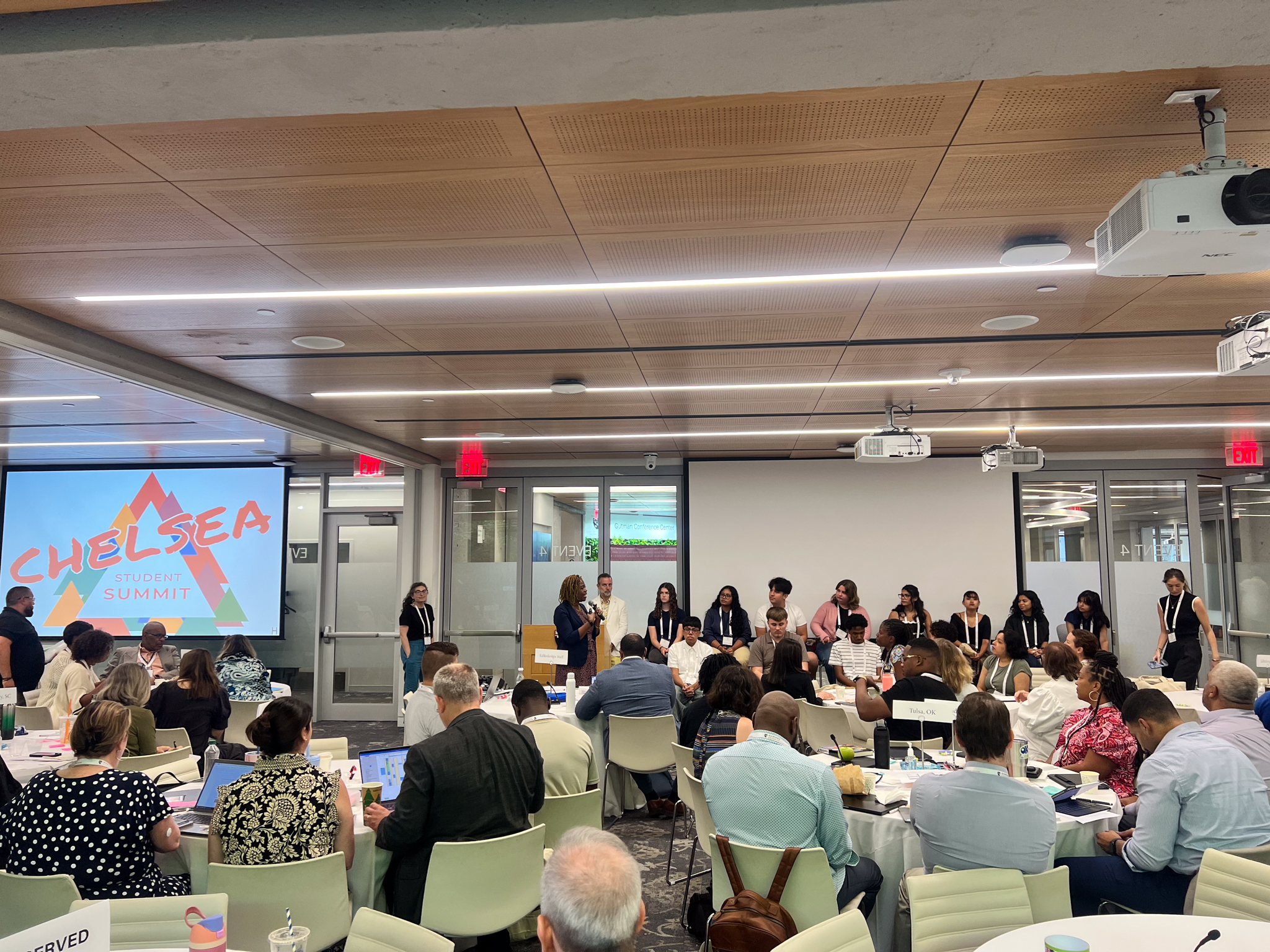 A picture from the back of the conference room of students from Chelsea speaking at a panel at Harvard